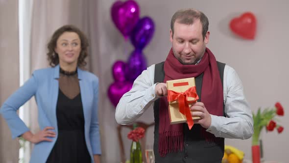 Excited Adult Man Opening Gift Box Posing with Expensive Watch As Blurred Smiling Woman Standing at