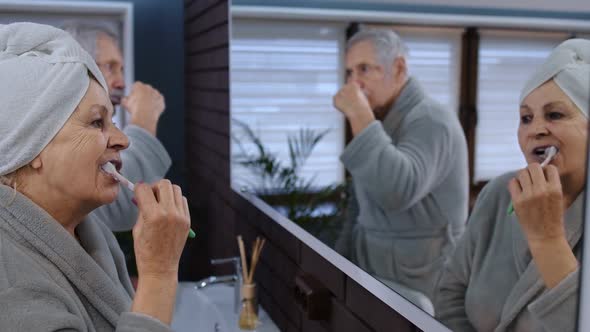 Senior Couple Grandmother and Grandfather Brushing Teeth and Looking Into a Mirror at Bathroom