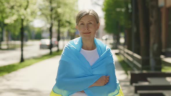 Mature Woman Carries a the Ukrainian Flag Standing on the Street Looking at the Camera on the