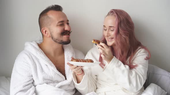 Woman Treats Man with Eclairs on Bed Have Breakfast Together