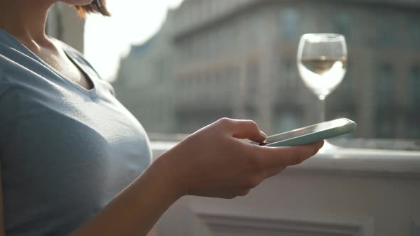 Close - Up of Young Woman's Hand Uses a Smartphone While Drinking Wine and Sitting By the Window