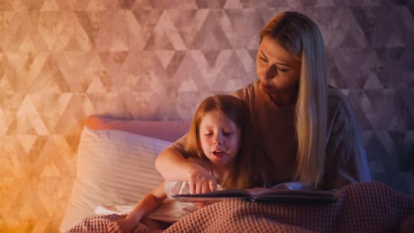 Mommy Teaches Girl to Read Following Line with Finger on Bed