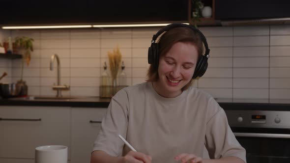 Beautiful Girl in Headphones Listens to Music Rejoices and Uses a Laptop in the Living Room