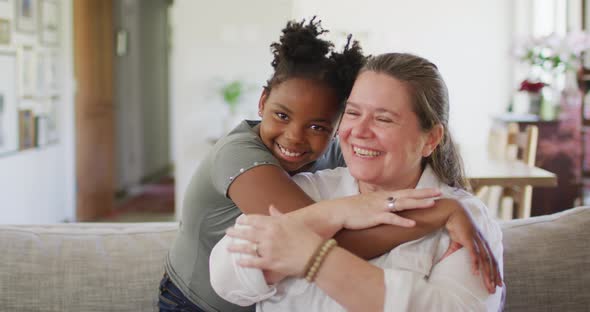 Portrait of happy caucasian woman and her african american daughter smiling in living room