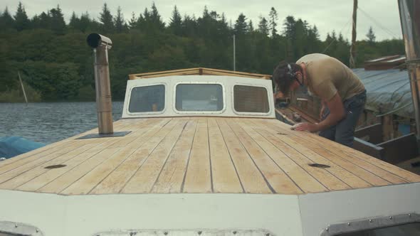 Young carpenter wiping down sanded deck of wooden liveaboard boat