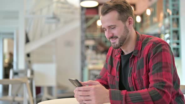 Attractive Young Man Using Smartphone in Cafe