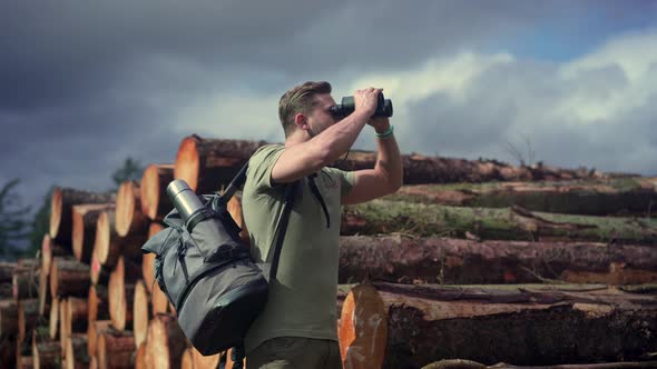 Hiker looking through binoculars at stack of wood