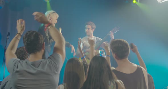 Man and woman singing and playing guitar in front of audience at nightclub