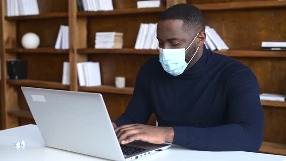 AfricanAmerican Male Employee Wearing Medical Mask Using Laptop Indoor