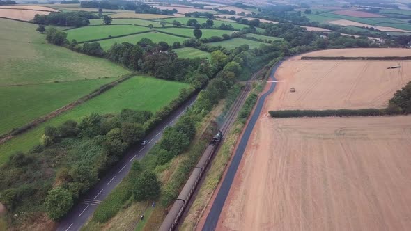 Aerial tracking forward over a Steam engineing forward out of a small station alongside a busy road