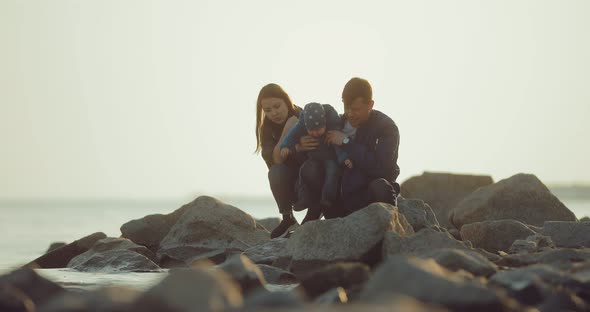 Husband Wife and Baby Sit on the Rocks on the Rocky Coast and Look Into the Distance