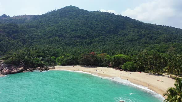 Exotic trees, sandy beach and turquoise sea water on the coast of Koh Phangan, Thailand. Aerial pano