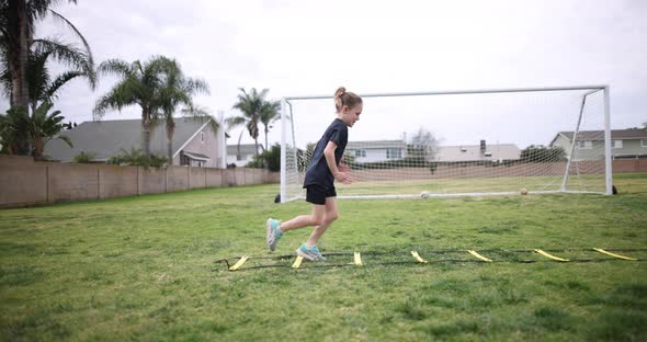 A young athletic girl does super fast feet on a speed ladder as she warms up for soccer practice.