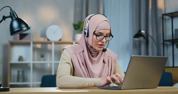 Muslim Girl in Hjab with Headset Working on Laptop at Home and then Looking into Camera