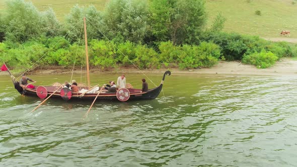 Vikings Sail on an Old Ship With a Lowered Sail on a Calm River
