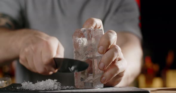 Bartender Makes Crushed Ice From Large Ice Cube By Sharp Knife Making the Cocktail on the Bar