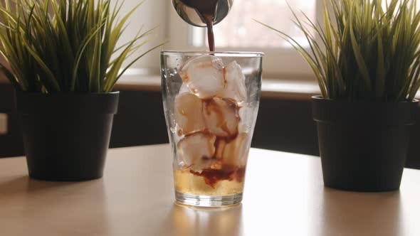 Barista Pours Coffee Into a Glass Cup with Ice Standing on a Table in a Cafe and Makes a Cocktail