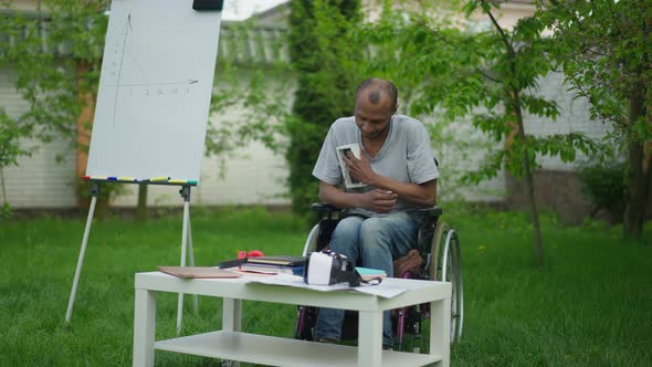 Depressed Paralyzed African American Man Hugging Photo Sitting in Wheelchair in Summer Garden