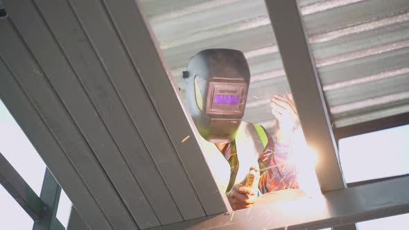 Asian construction builder male welder is welding steel beams in process of home renovation.