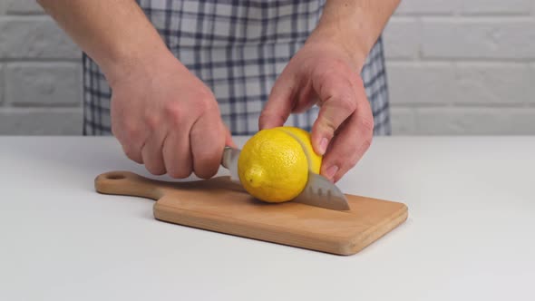 Male hands cut lemon in half on cutting board.