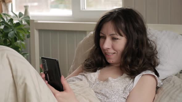 Woman Lying in Bed in Morning and Looking at Phone
