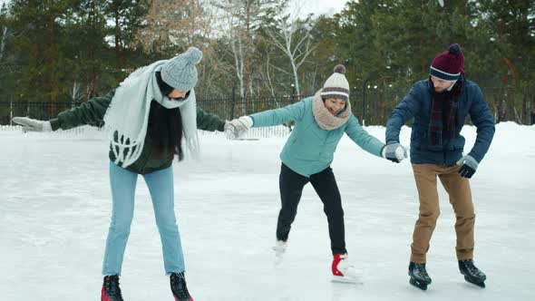 Friends Teaching Young Woman To Ice-skate in Winter Park but Amateur Falling and Laughing