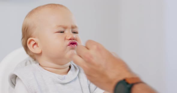 Closeup of Young Baby in White High Baby Chair and Father's Hand with a Cake While He is Feeding the