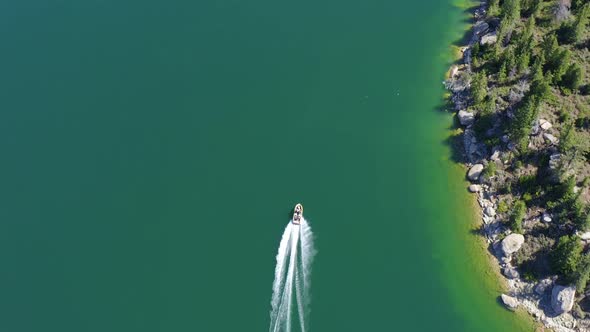 Aerial bird's eye view of a boat motoring along the shoreline of a clear, blue lake