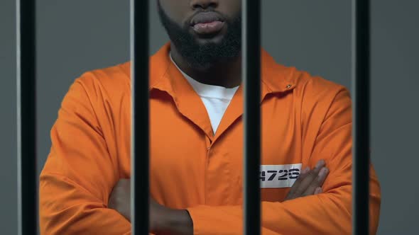 Black Criminal With Hands Crossed Standing in Prison Cell, Waiting for Judgment