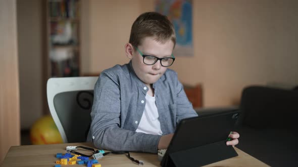 Boy in Glasses Sits at Table Taps on Tablet Learns to Create Toy Robot
