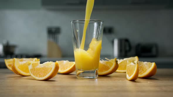 Orange juice is poured into glass on wooden table with orange slices on it in the kitchen. Close up