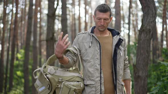 Portrait of Confident Caucasian Man Taking Off Backpack Looking Around Standing in Sunny Forest