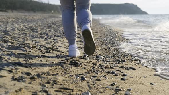 Closeup of the Legs of a Runner Running Along the Beach and Dodging the Waves