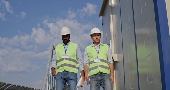 Mixed Race Male Engineers Walking Down Stairs of Technical Building. Two Man in Hard Helmet and