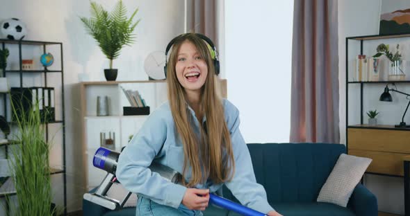 Girl in Headphones which Listening Favourite Music and Playing on Vacuum Cleaner Like a guitar