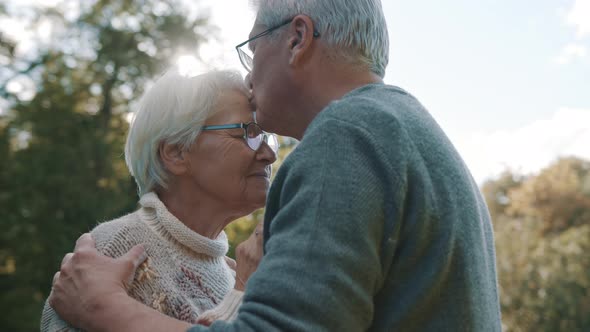 Happy Old Couple Dancing at Autumn Park. Senior Man Flirting with Elderly Woman. Kiss in Forehead in