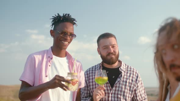 Team of Cheerful Friends are Standing Against Background of Field and Drinking Cocktails