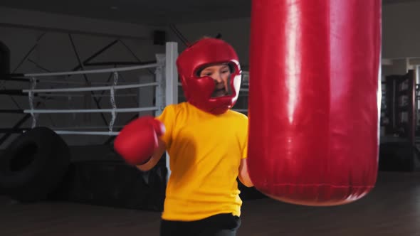 Little Boy in Protective Helmet Kicking the Punching Bag From the Turn