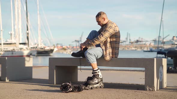 Stylish man putting on roller skates on embankment