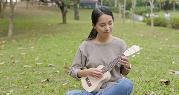Asian Woman enjoy play ukulele and song in the park
