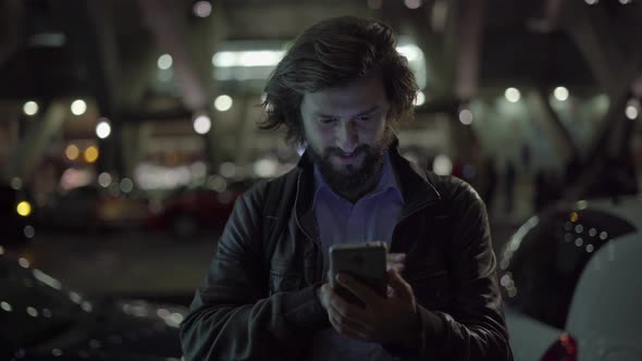 Smiling Caucasian Man Using Gadget at Night in Urban City