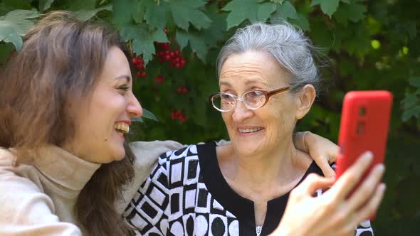 Adult Daughter and Senior Mum are Taking Selfportrait Picture Selfie on Red Smartphone Together