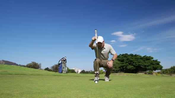 Caucasian male golfer kneeling on a golf course on a sunny day