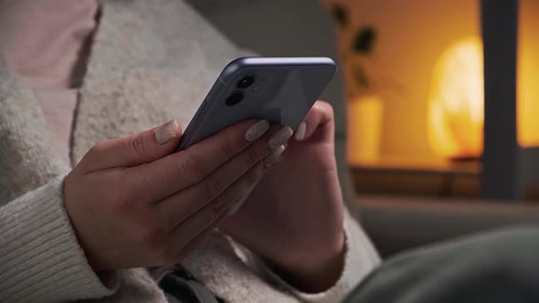 Close Up Woman Hands Using Mobile Phone in Very Peri Color While Sitting in Armchair at Home in