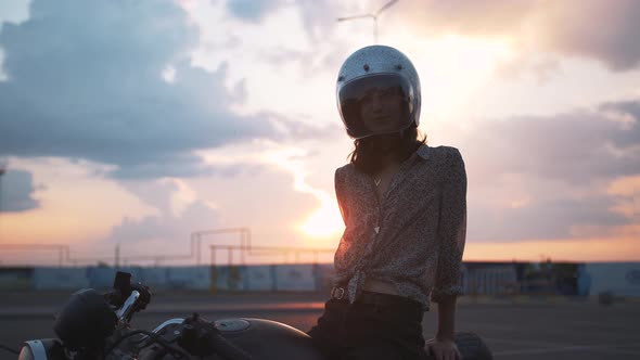 Beautiful Young Woman Motorcyclist with Helmet on Beautiful Sunset Sky Background