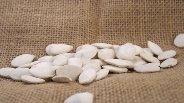 Dry salted pumpkin seeds with shells fall on a rustic sack in slow motion