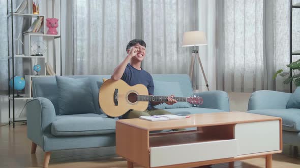 Asian Boy Composer With A Guitar Celebrating For Finishing Composing Music On Paper At Home