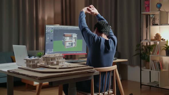 Asian Male Engineer Stretching While Designing House On A Desktop At Home