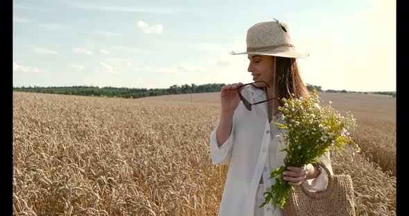 Stylish Woman with Bunch of Flowers in Wheat Field