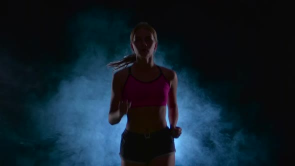 Girl Fitness Runs Steadily. Front View. Black Screen in the Smoke. Silhouette. Slow Motion. Close Up